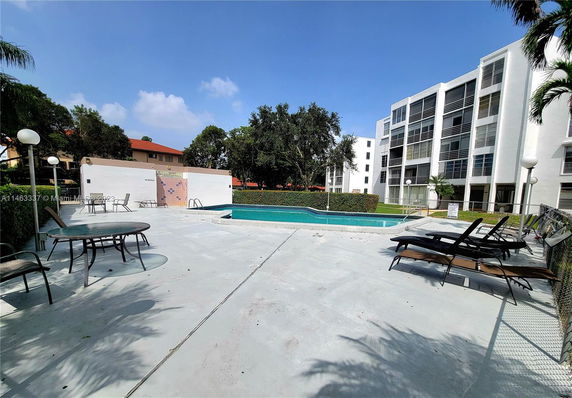 Outdoor swimming pool area with lounge chairs and tables near a residential building.