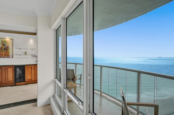 View from a balcony overlooking the ocean with glass railing and clear blue sky.