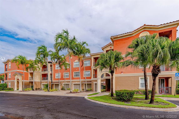 Front view of a multi-story apartment building with balconies and a stucco exterior.