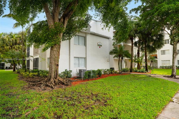 Front view of a multi-story white apartment building with trees and green lawn.