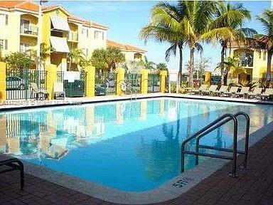 Outdoor swimming pool surrounded by yellow buildings and palm trees.