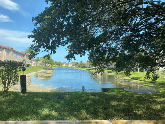 View of a pond surrounded by residential buildings with red roofs and green lawns.