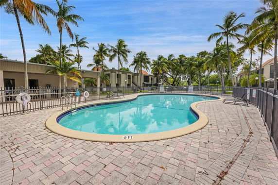 Outdoor swimming pool with surrounding palm trees and residential buildings.