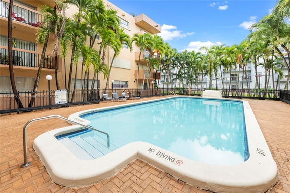 Outdoor swimming pool in an apartment complex with surrounding palm trees and balconies.