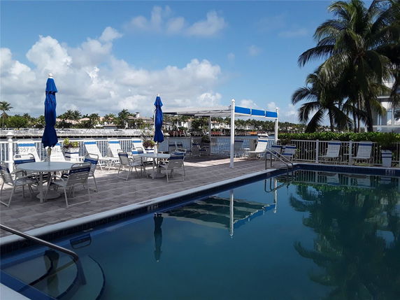 Outdoor swimming pool area with tables, chairs, and umbrellas.