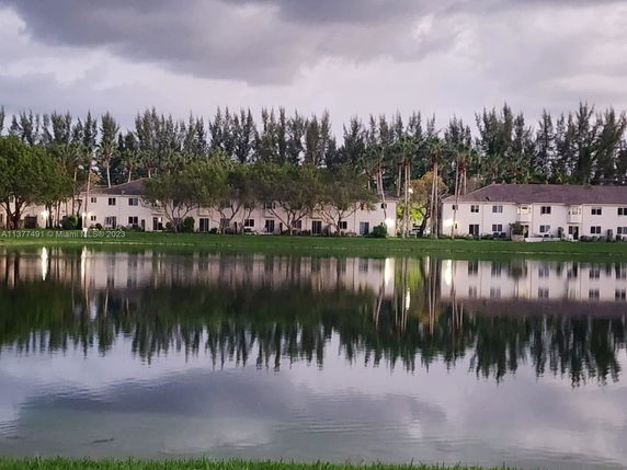View of a row of two-story buildings with a lake and trees in the foreground.