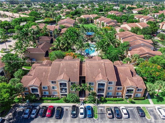 Aerial view of apartment complex with multiple buildings, a central swimming pool, and landscaped greenery.