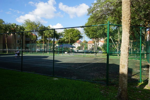Outdoor tennis court surrounded by a chain-link fence in a park or community area.