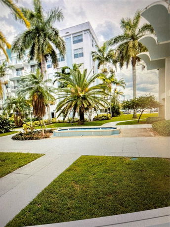 View of a multi-story building with palm trees and a small fountain in the foreground.