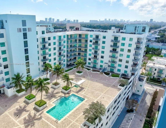 Aerial view of a multi-story residential building with a central swimming pool and surrounding palm trees.