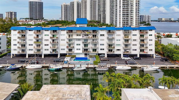 Front view of a multi-story apartment building with balconies and a waterfront.