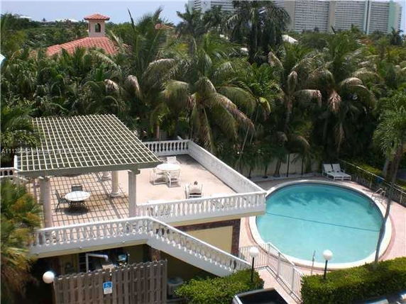 View of a swimming pool next to a rooftop area with lounge chairs and a pergola.