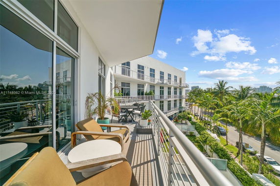 View from a balcony of a multi-story building with palm trees lining the street.