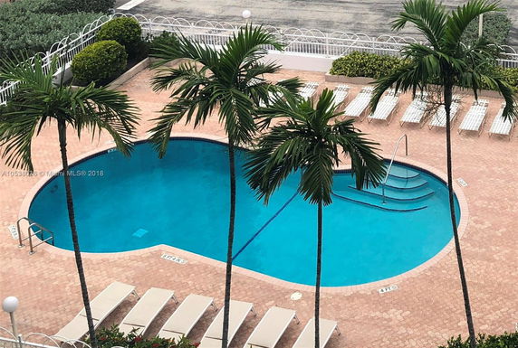 View of a swimming pool with surrounding lounge chairs and palm trees.