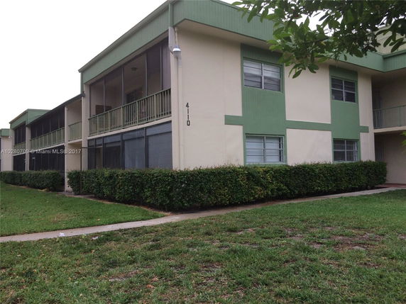 Front view of a two-story residential building with green trim and screened balconies.