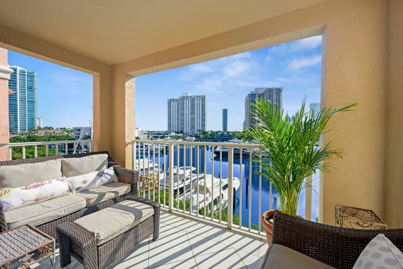 Balcony with outdoor seating overlooking a marina and city skyline.