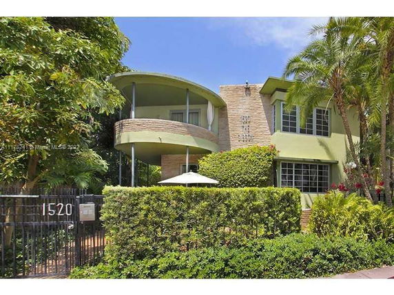 Front view of a two-story house with a curved balcony and surrounding greenery.