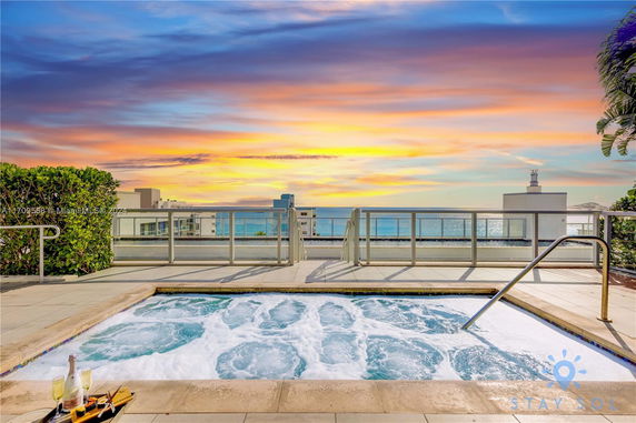 Rooftop with a hot tub and ocean view, featuring a clear sky at sunset.