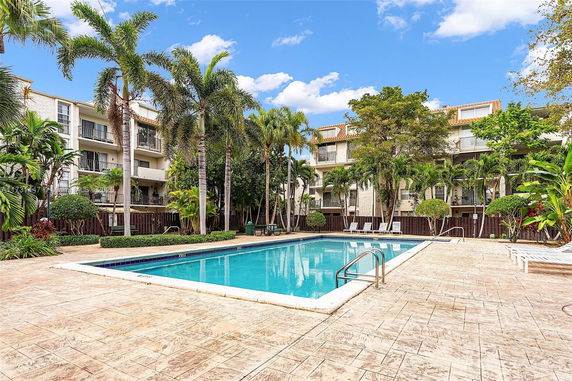 Outdoor swimming pool area in front of a residential building with palm trees