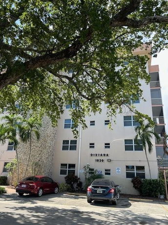 Front view of a multi-story apartment building with a tree in the foreground.