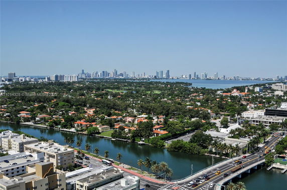 Panoramic view of a city with a mix of residential and high-rise buildings near water and greenery.