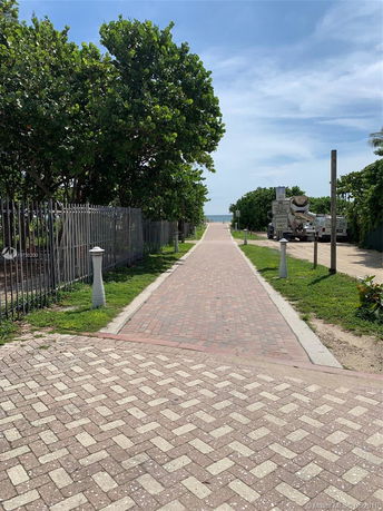Pathway leading to the beach, lined with trees and fencing.