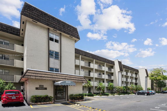 Front view of a multi-story residential building with covered entrance and parking area.