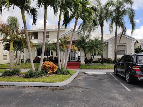 Front view of a two-story house with palm trees and a red pathway.