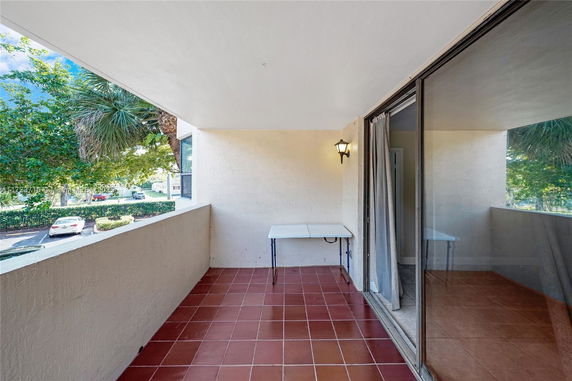 Covered outdoor balcony area with a table, featuring views of trees and parked cars.