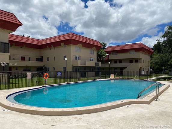 Outdoor swimming pool in front of a multi-story building with red roofs.