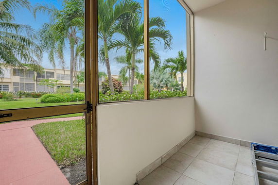 View of surrounding garden area from a screened porch with palm trees visible outside.