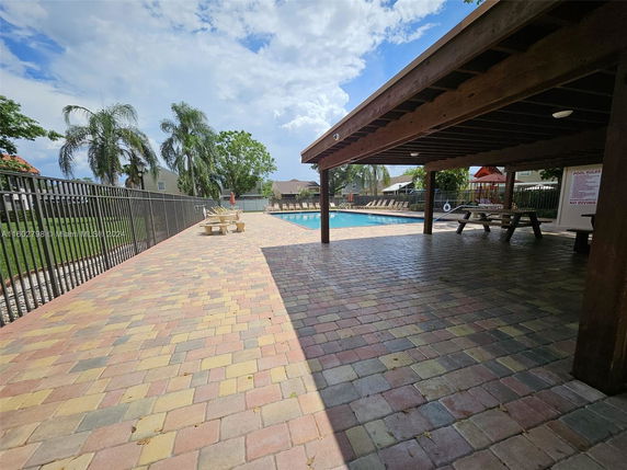 Outdoor swimming pool area with paved tiles and covered seating.