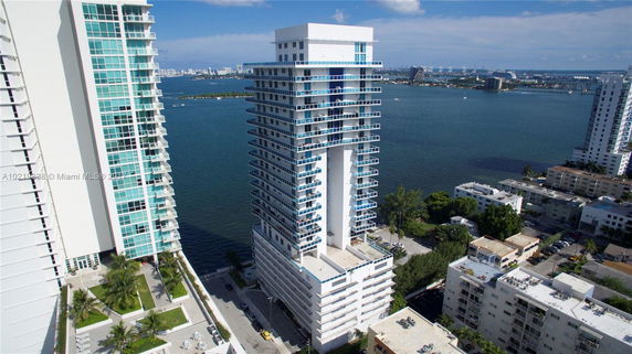 High-rise building near a large body of water, with other buildings and greenery in the background.