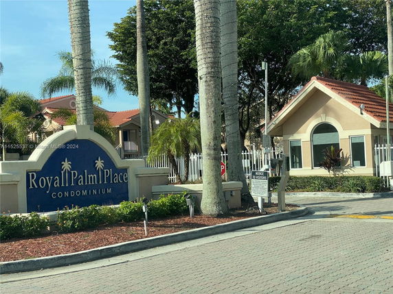 Front view of a condominium entrance with signage and a small building.