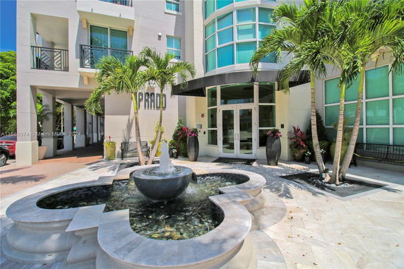 Front view of a modern building entrance with a fountain and palm trees.