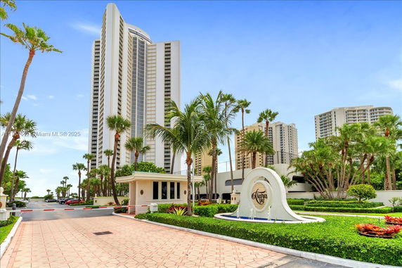 Front view of a tall residential building with a curved facade and surrounding palm trees.