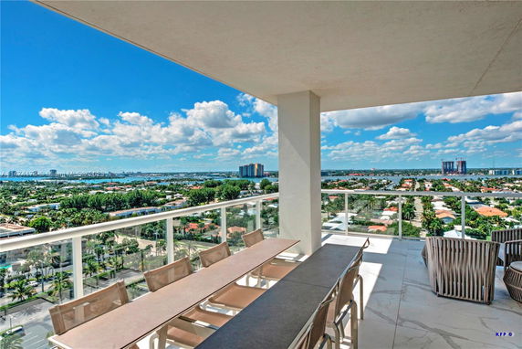 Panoramic view from a high-rise apartment balcony, showcasing cityscape and distant water bodies.