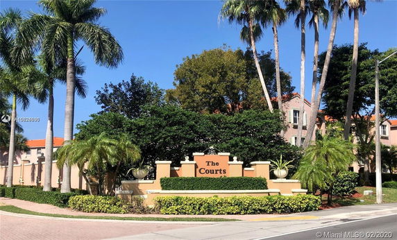 Front view of a residential complex with palm trees and a sign reading 'The Courts'.