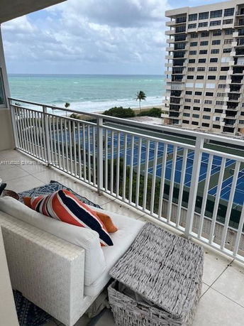 Panoramic view from a balcony overlooking the ocean and tennis courts, with a multi-story building nearby.
