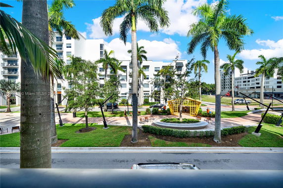 View of white multi-story residential buildings with palm trees and a small park area.