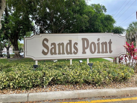 Sign displaying the name 'Sands Point' with greenery and trees in the background.
