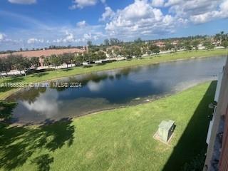 View of a grassy area and pond with trees and buildings in the background.