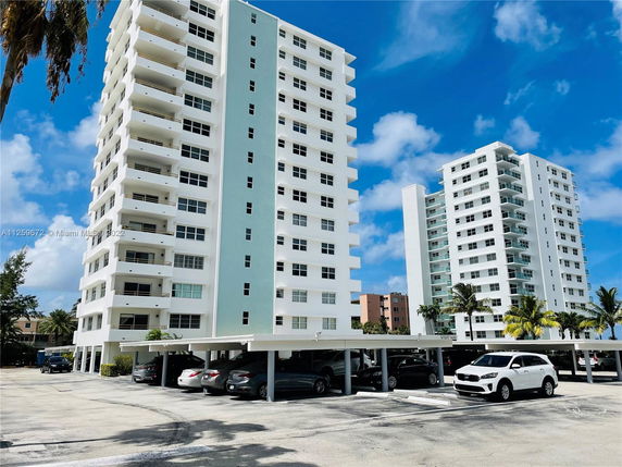 Front view of a high-rise apartment building with balconies and a parking area.