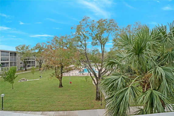 View of an outdoor area with grass, trees, and a pool, surrounded by buildings.