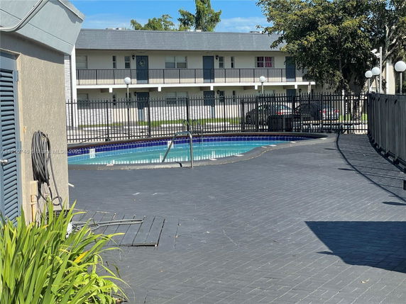 Outdoor swimming pool with tiled surroundings and a fence.