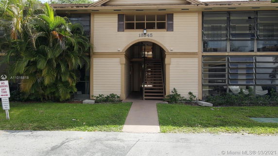Front view of a two-story building with an entrance archway and surrounding greenery.