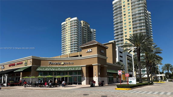 Front view of a commercial building with multiple storefronts and high-rise buildings in the background.