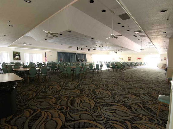 Interior view of a large club house room with tables, chairs, and a stage.