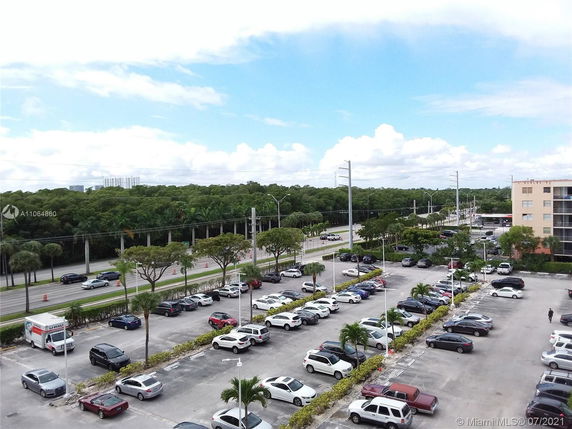 View of a parking lot with several cars and a road bordered by trees.