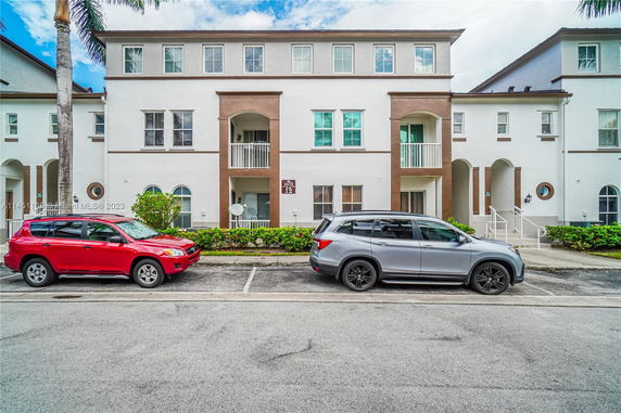 Front view of a multi-story residential building with parked cars.